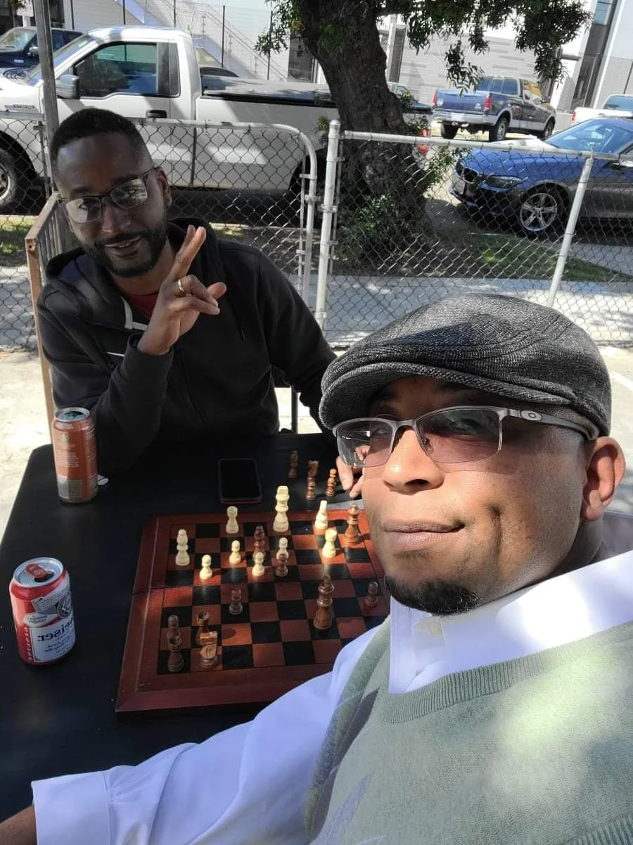 Donyale DThree Mack wearing a hat in the foreground, with his brother Davion across the chessboard.